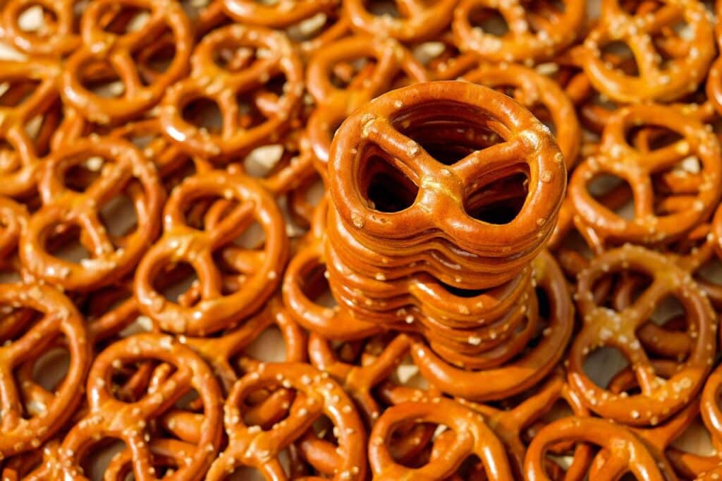 A ton of pretzels on a table, and about ten of them stacked in the center.
